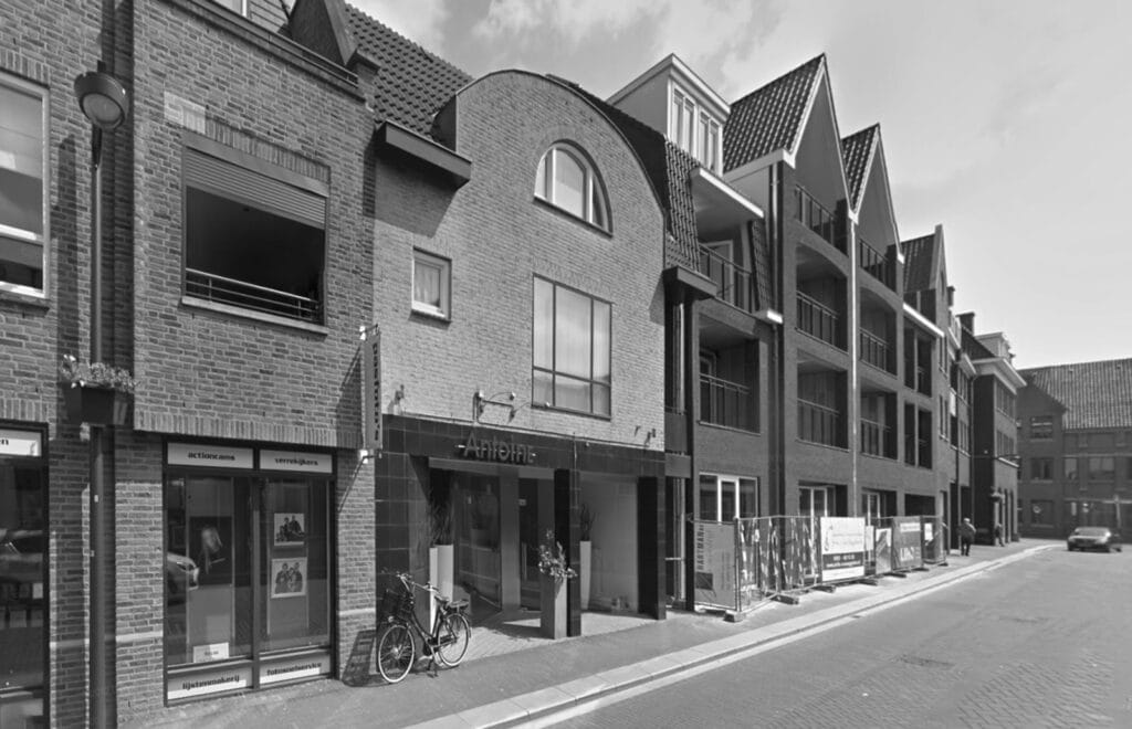 Gemetselde halfronde kopgevel, bakgoten, keramische dakpannen, inpandig etalageraam, perspectief schuin vanuit winkelstraat-optoppen-gebouw