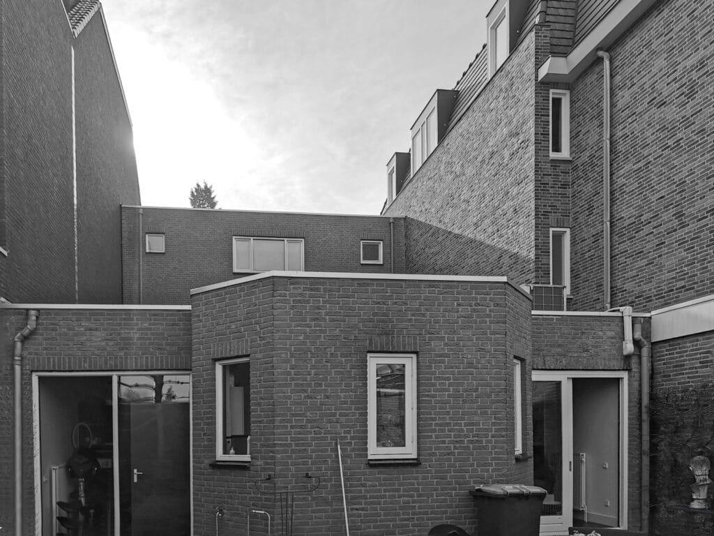 Uitgebouwde achtergevel: metselwerk, smalle ramen, dubbele deuren, ingeklemd tussen belending en blinde wanden.