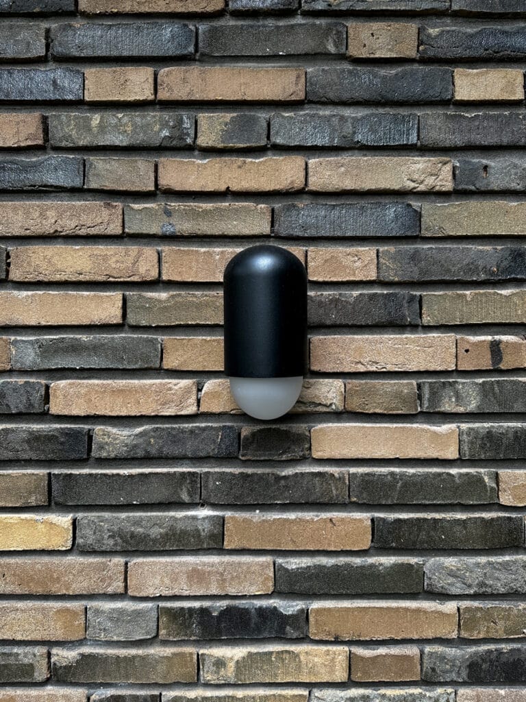 Bruin-zwart metselwerk met smalle stootvoegen, horizontale nadruk, blinde moderne wandlamp.