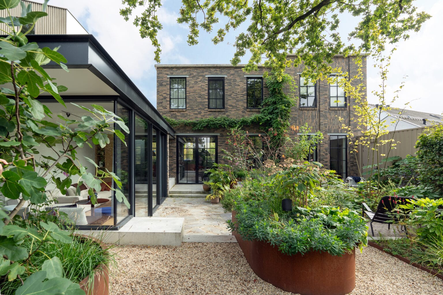 moderne uitbouw vrijstaande woning met Schüco hefschuifpui met glazen hoek, betonnen zitelement, UMP profiel dakrand, cortenstaal, beton, staal, glas.