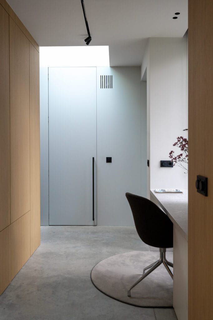 Interieur werkkamer: blinde deur technische ruimte, daglicht over bureau, houten kastenwand, lichtblauwe achterwand, strak gedetailleerd daklicht, geïntegreerde plafondverlichting.