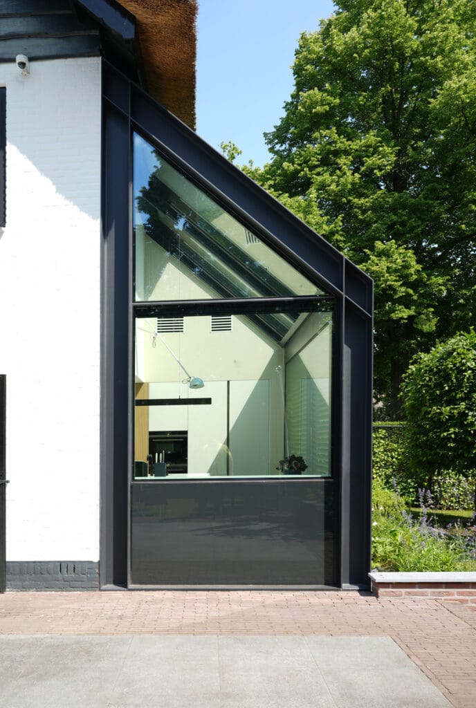 --- Moderne hightech uitbreiding met antraciet staal en glas naast gekeimde woning, hout, rieten kap.