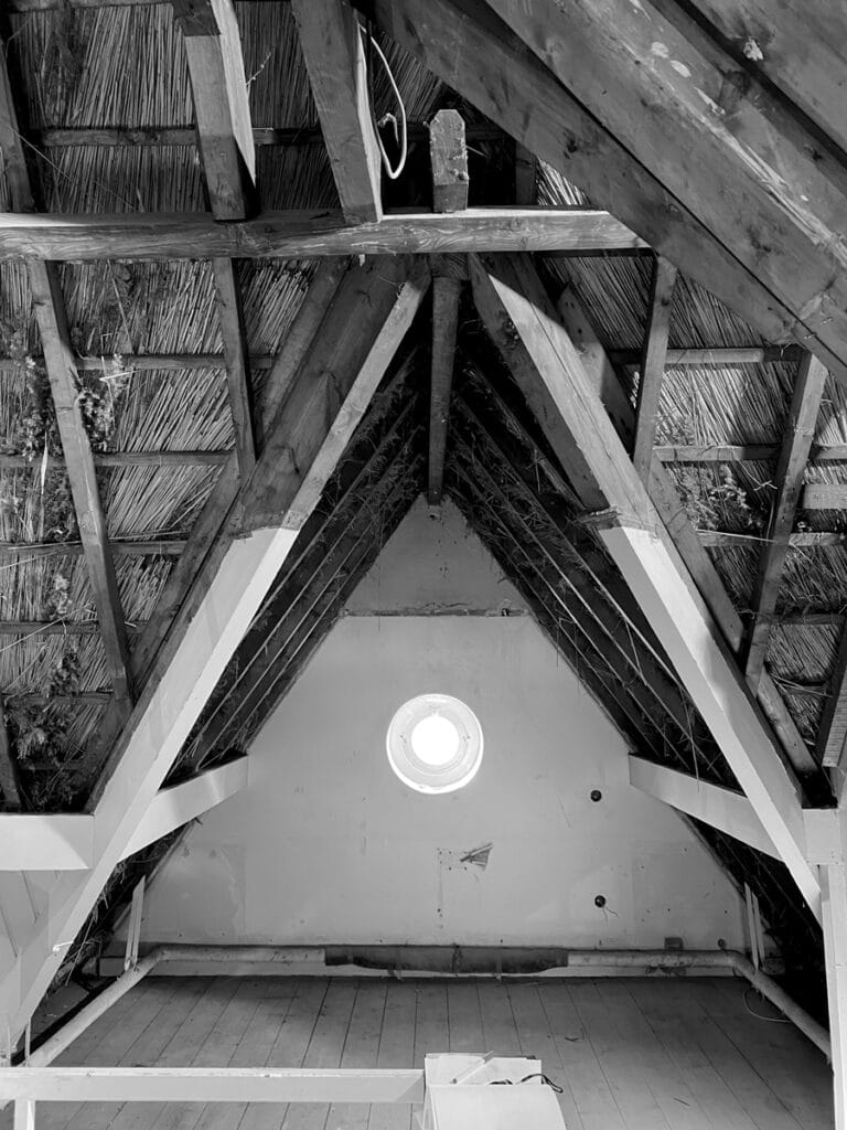 Zolder Karel de Bazel: perspectief kopgevel, oculus raam, zichtbare houten constructie en rieten dak.