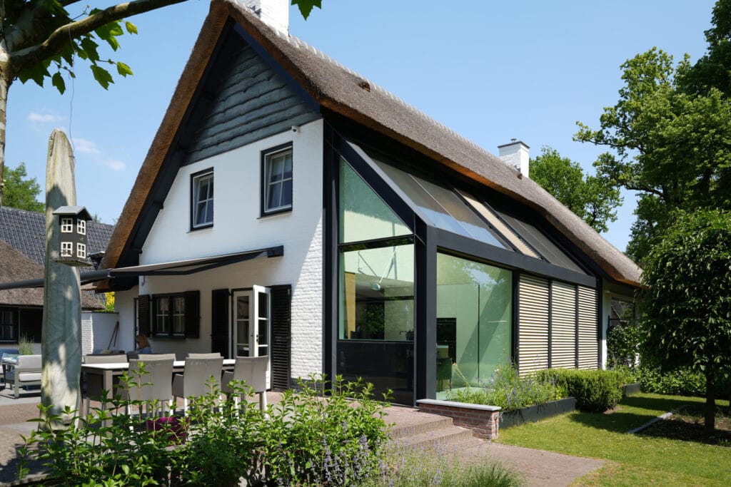 Uitbouw met staal en glas-antraciet staal, glasdak, geautomatiseerde zonwering; naast gekeimde woning, hout, rieten kap.