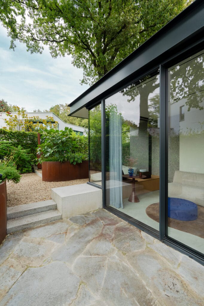 Schüco hefschuifpui met glazen hoek, betonnen zitelement, UMP profiel dakrand, combinatie cortenstaal, beton, staal en glas.