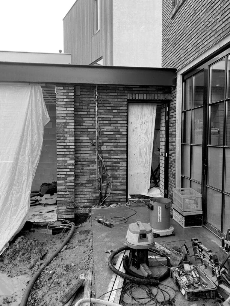 Bestaande metselwerk uitbouw, stootvoegloos penant, betonnen terrasvloer, glazen tuindeuren, stalen UNP-balk als tuinkamer dakrand.