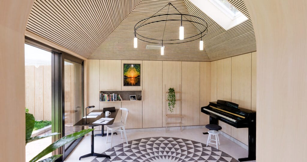 Muziekstudio met akoestisch houten dak, geometrische vloer en ingebouwd bureau.