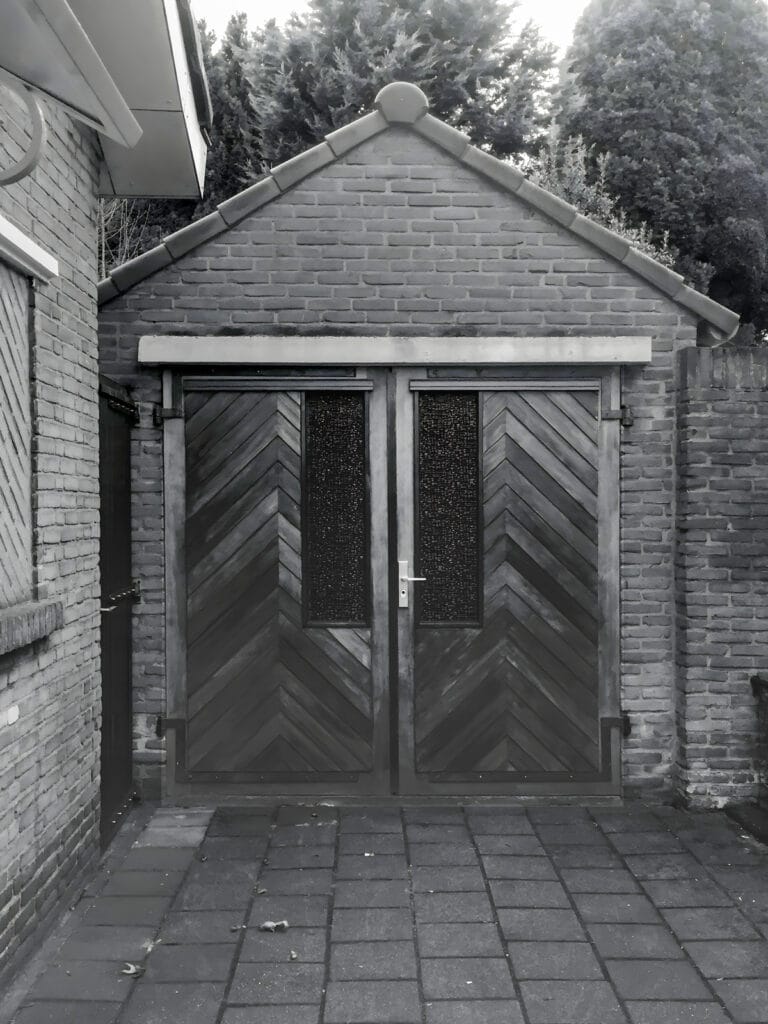 Dubbele garagedeur kopgevel verouderde garage met toegangsdeur achtertuin.