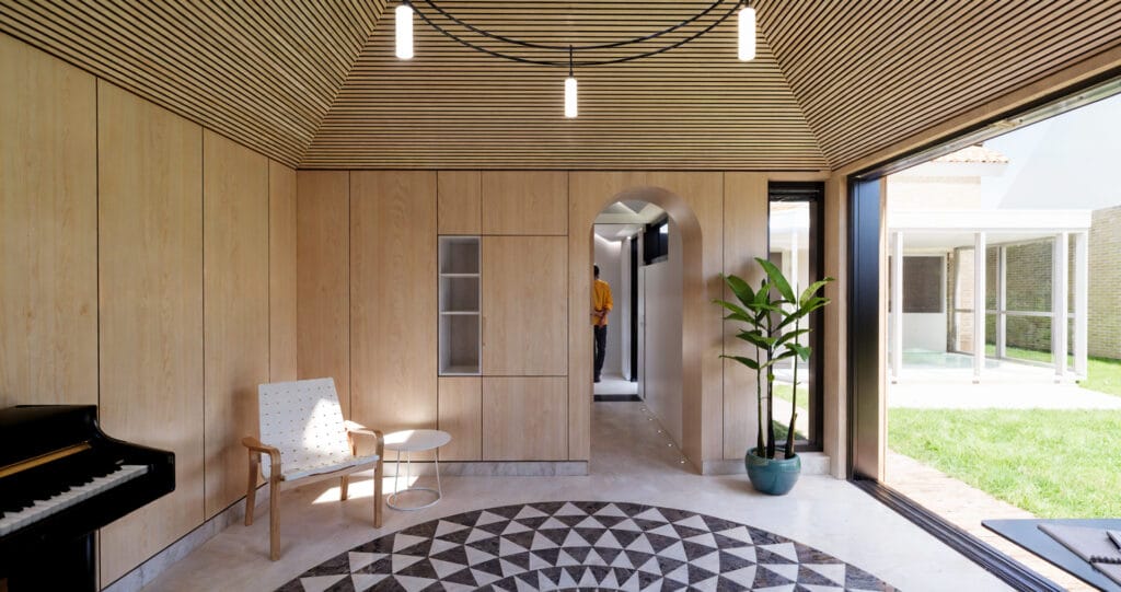 Muziekstudio met akoestisch houten dak, geometrische vloer en ingebouwd bureau.