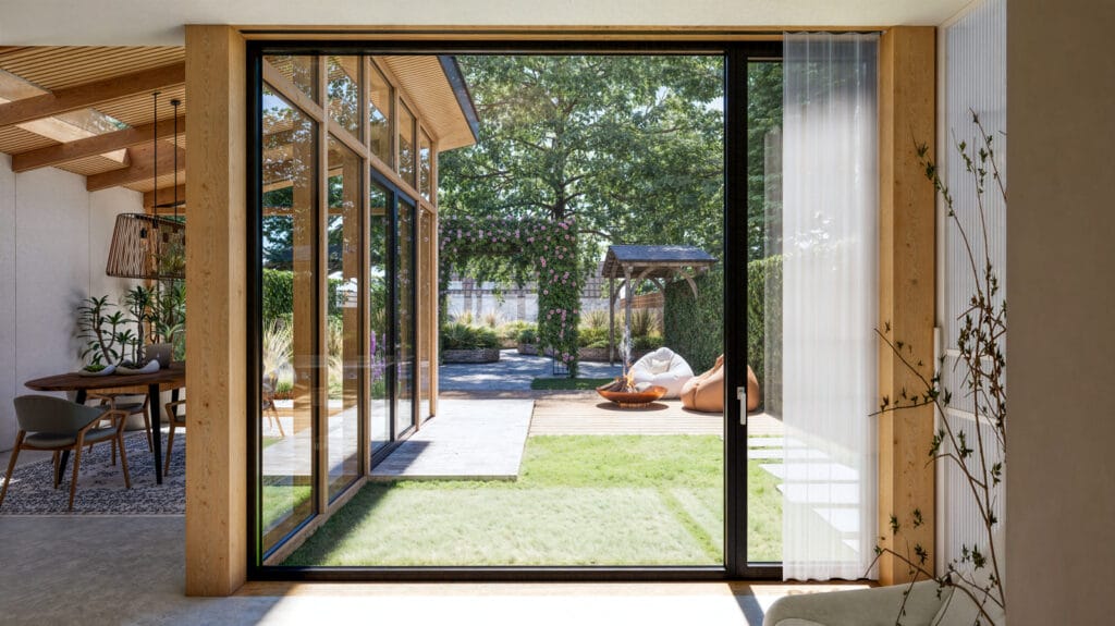 uitbouw jaren 30 woning strak gedetailleerd, verdiepingshoog raam met slanke profielen tussen houten kolommen, biedt volledig zicht op tuin en hoge boom. Vierkante uitvoering met draai-kiep zijlicht voor natuurlijke ventilatie en mooie verhoudingen.